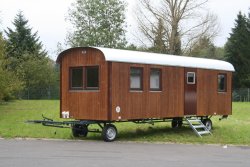 WEIRO® forest kindergarten trailer with 8 m long body, roof overhang, dark varnish finish, and with wood tilt and turn windows.