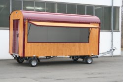 <h5>WEIRO® sales trailer</h5>with 5 m body length, two–axle chassis with ball hitch, wood outer paneling, overhead door on side, and entryway at the rear.