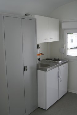 Furnishing example with small kitchen with electric hotplates, stainless steel sink and refrigerator, high cupboard and an additional material cabinet.
